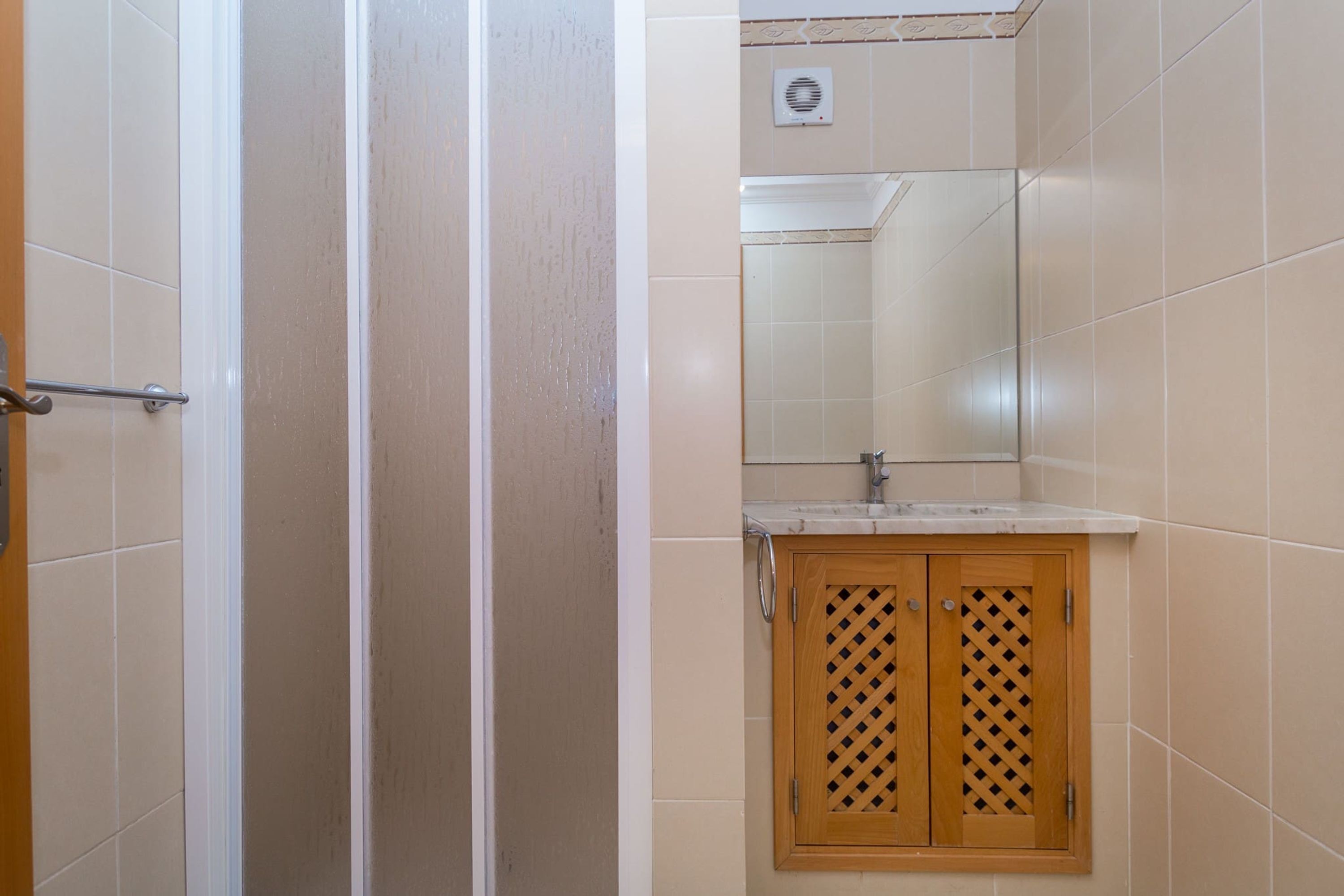 A bathroom with a shower, a sink, and a wooden cabinet.