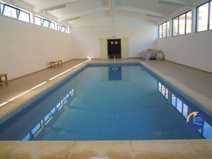 Ein Innenpool mit klarem, blauem Wasser, Fliesenboden und einer Decke mit Oberlichtern.