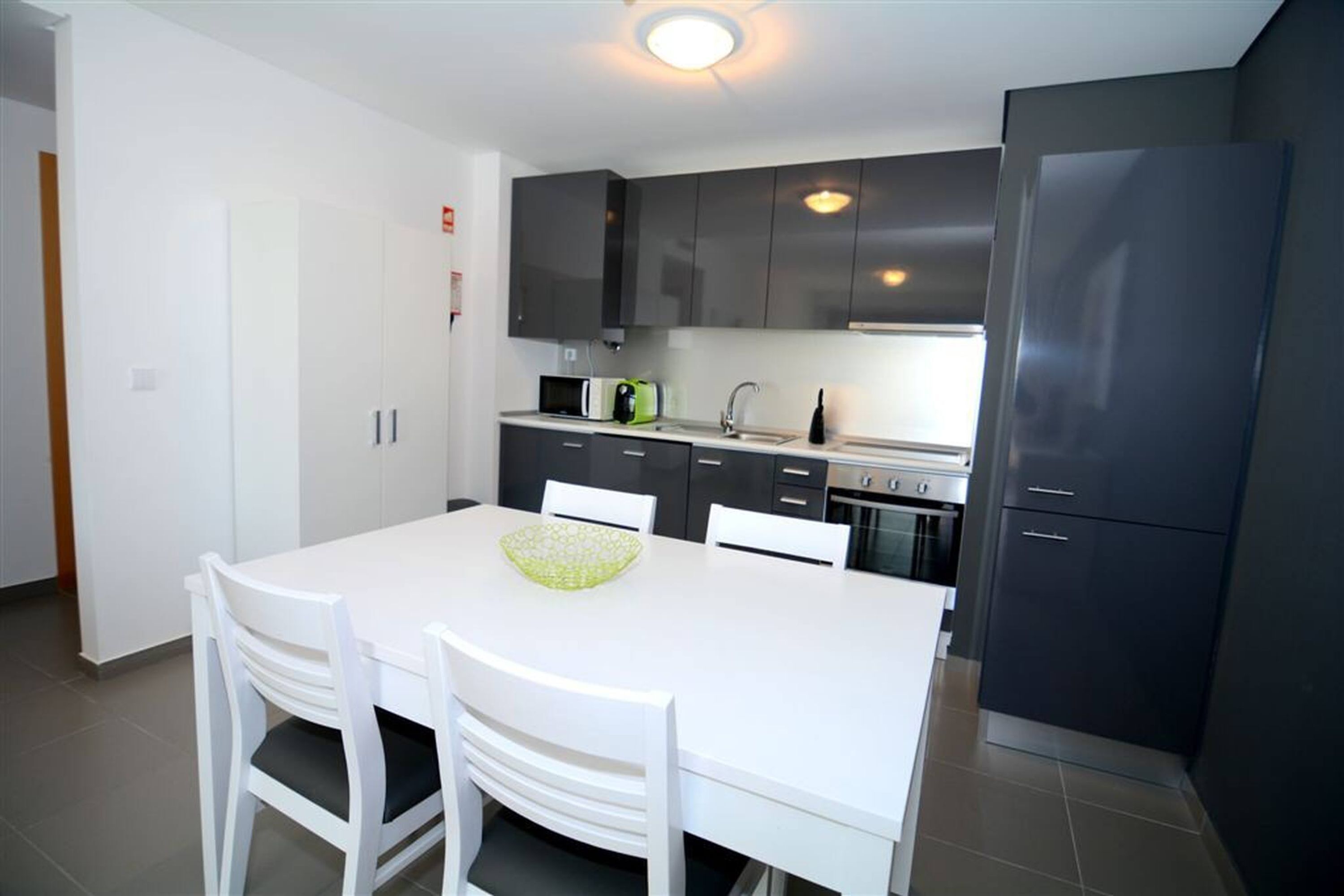A modern kitchen with dark cabinets, a white dining table, and chairs.