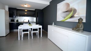 A modern kitchen with white cabinetry, a dining area with a white table and chairs, and a decorative Buddha statue on a white console table. - 09 - B707 in Portim o (Portimão)