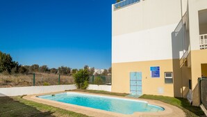A swimming pool with a clear blue sky, a building with a white and yellow facade, and a fenced area with greenery. - 30 (Portimão)
