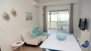 A modern living room with a white sofa, teal cushions, a white table with a teal bowl, and a TV on a cabinet. - 30 (Portimão)