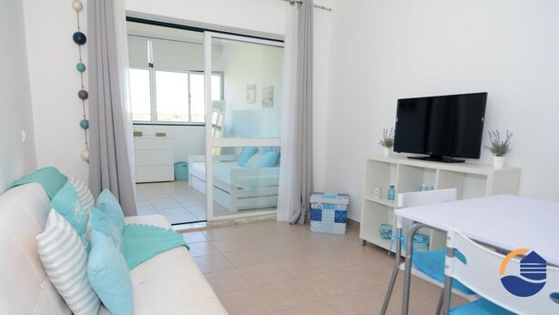 A modern living room with a white sofa, teal cushions, a flat-screen TV, and a dining area with a table and chairs. - 30 (Portimão)