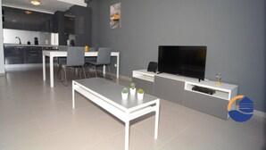 A modern living room with a flat-screen TV, a dining area with a white table and chairs, and a kitchen in the background. - 16 - B709 in Portim o (Portimão)