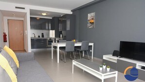 A modern living room with a grey sofa, a dining area with a white table and chairs, a kitchen in the background, and a flat-screen TV on a stand. - 16 - B709 in Portim o (Portimão)