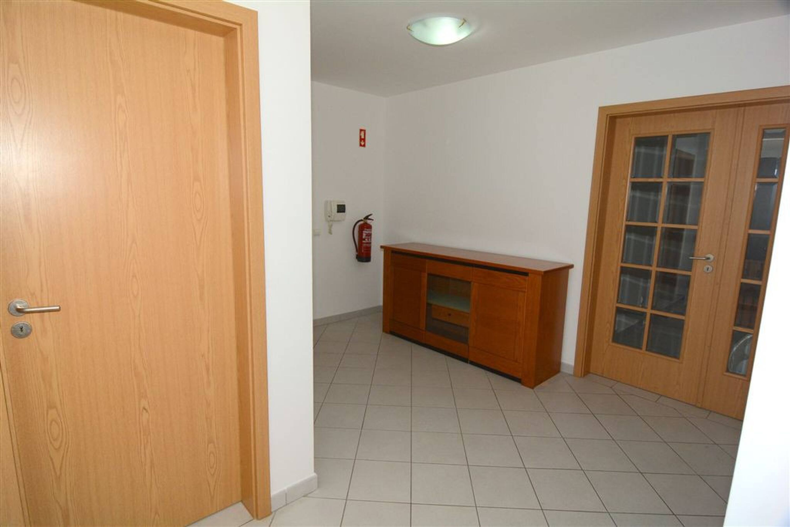 Ein Zimmer mit Holztür, Holzschrank, Fliesenboden und Feuerlöscher an der Wand.
