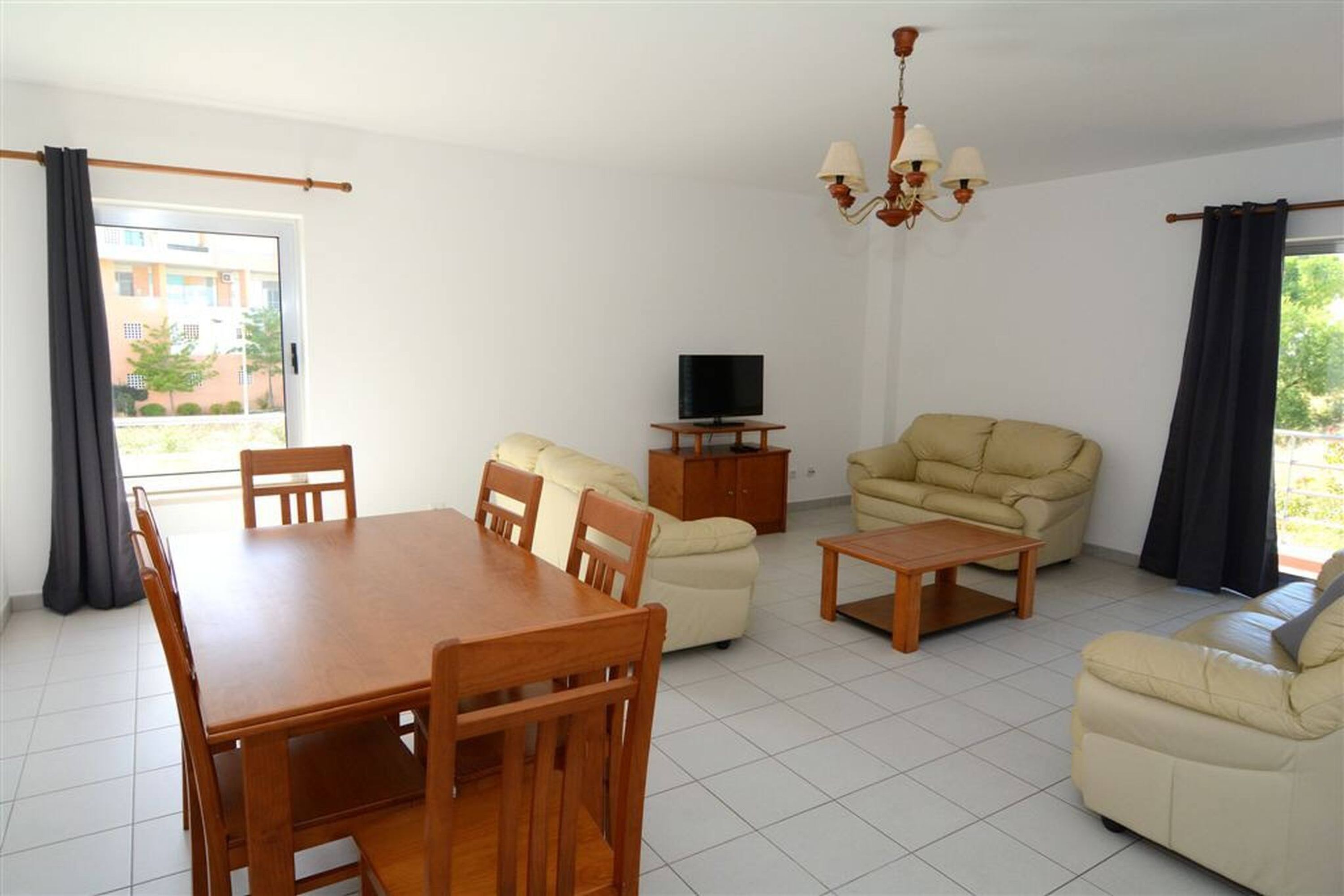 A living room with a dining table, sofas, a TV, and a chandelier.