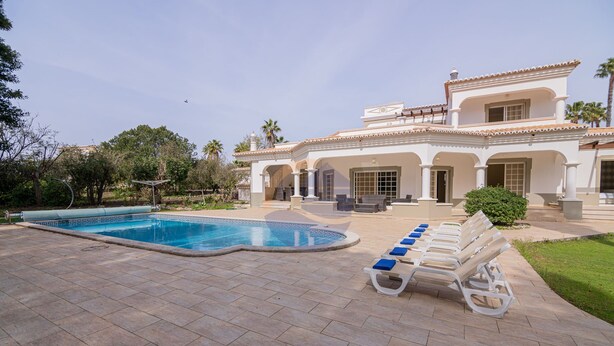 A pool area with lounge chairs and a large house in the background.
