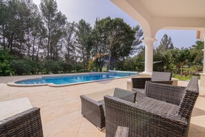A covered outdoor area with a swimming pool, wicker furniture, and a view of trees. - 80 (Portimão)