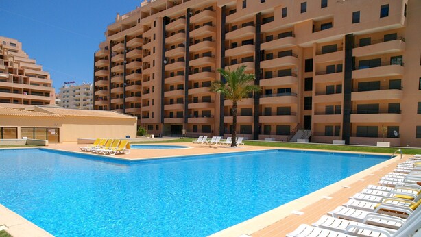 A swimming pool with lounge chairs and a palm tree, surrounded by a multi-story building. - 01 - B206 in Portim o (Portimão)