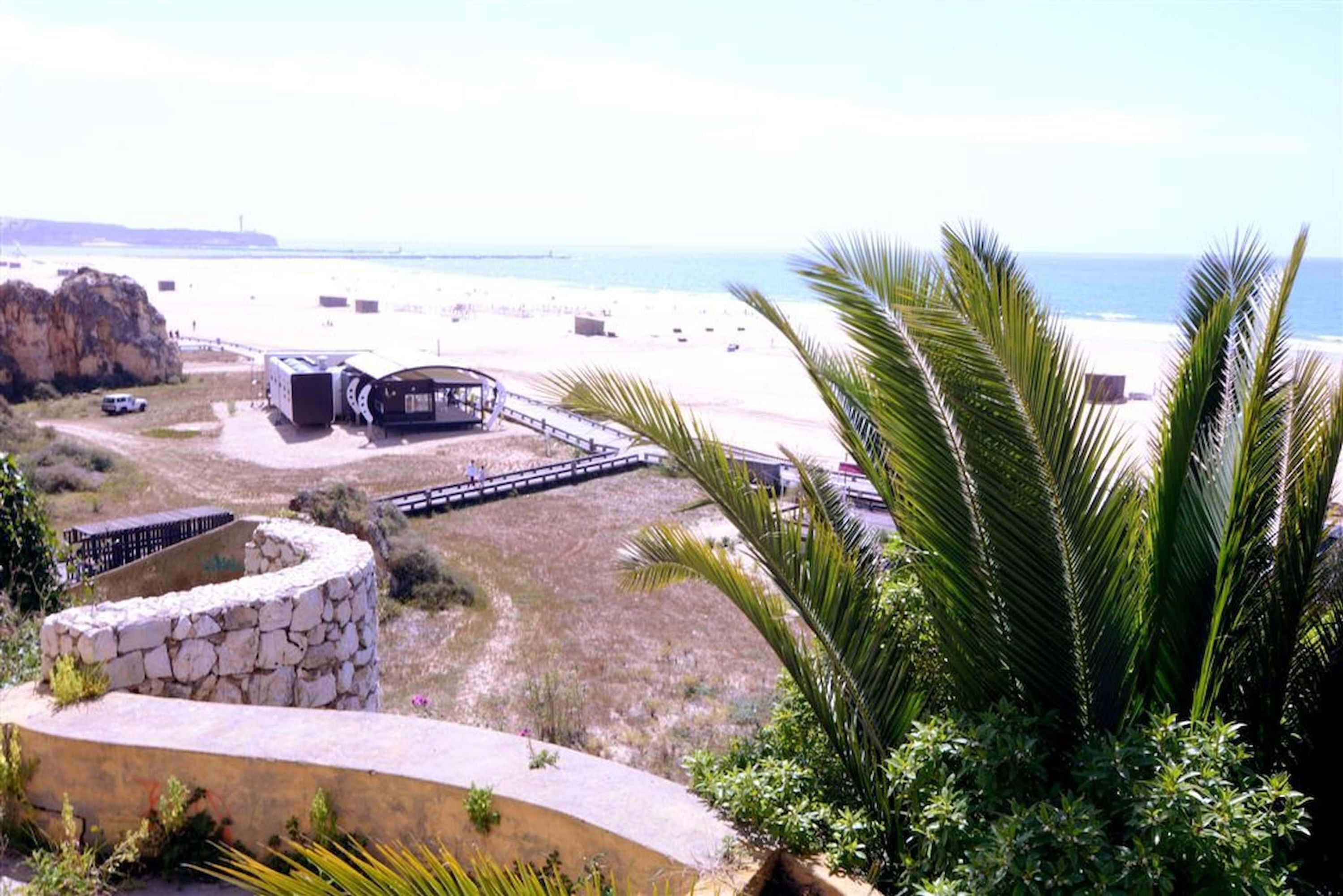 Blick auf die Küste mit Strand, einer Steinstruktur und einem Holzsteg, der zum Strand führt.