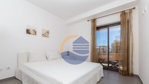 Ett hotellrum med en stor säng, en balkong med utsikt över staden och två konstverk som hänger på väggen.