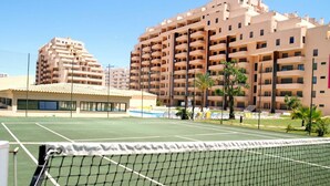En tennisbana med ett nät i förgrunden, omgiven av flerfamiljshus.