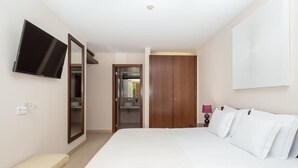 A bedroom with a bed, a TV mounted on the wall, a wardrobe, and a bathroom visible through an open door.