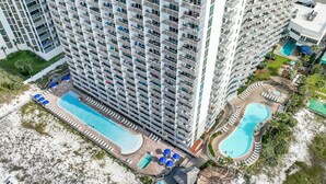 Un hôtel de grande hauteur doté de nombreux balcons, d’une grande piscine et d’un espace piscine séparé avec des chaises longues et des parasols.