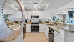 Une cuisine moderne avec des meubles blancs, des appareils en acier inoxydable et un miroir circulaire original orné de clous métalliques.