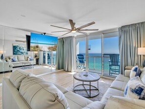 Un salon spacieux avec un grand canapé, une table basse et un balcon offrant une vue sur l’océan.