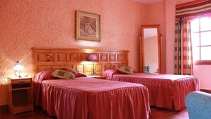 Ein Zimmer mit zwei Betten, einem Holz-Kopfstück, einem Nachttisch mit Lampe, einem gerahmten Bild an der Wand und einem Fenster mit Vorhängen.