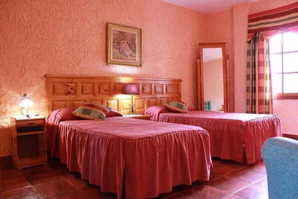A room with two beds, a wooden headboard, a nightstand with a lamp, a framed picture on the wall, and a window with curtains.