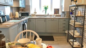 Cocina moderna con armarios grises, una isla central y zona de desayuno con frutas, croissants y café.
