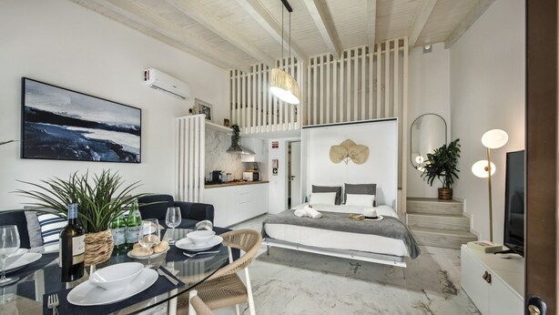 A modern hotel room with a dining area, a bed with a gray and white color scheme, a large painting on the wall, and a staircase leading to an upper level. - Alca Arias Suite 20 (Faro)