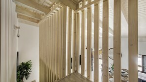 A modern interior with wooden slats, a plant, and a dining area with wicker furniture. - Alca Arias Suite 20 (Faro)