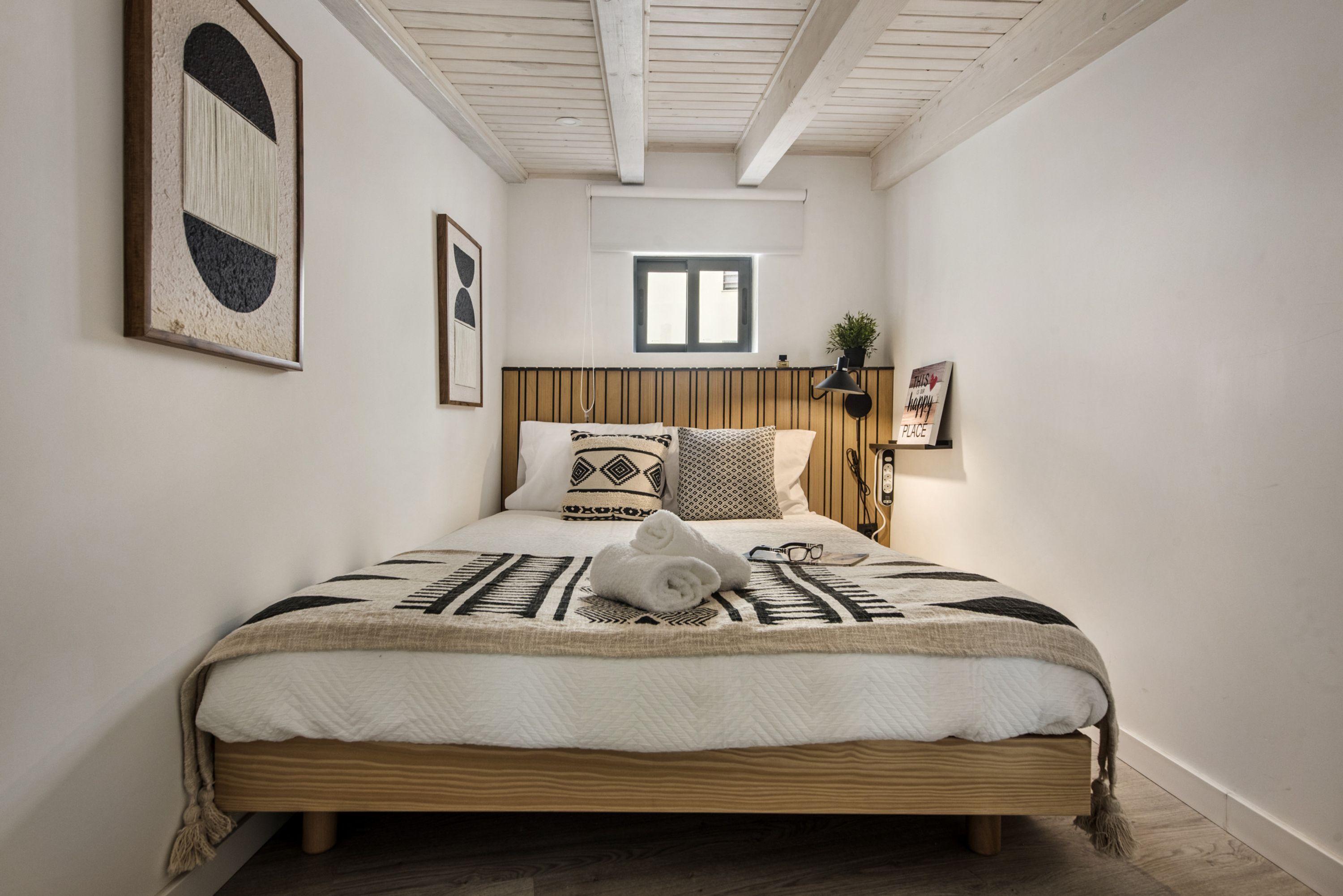A bedroom with a wooden bed, a window, and a wall-mounted plant.