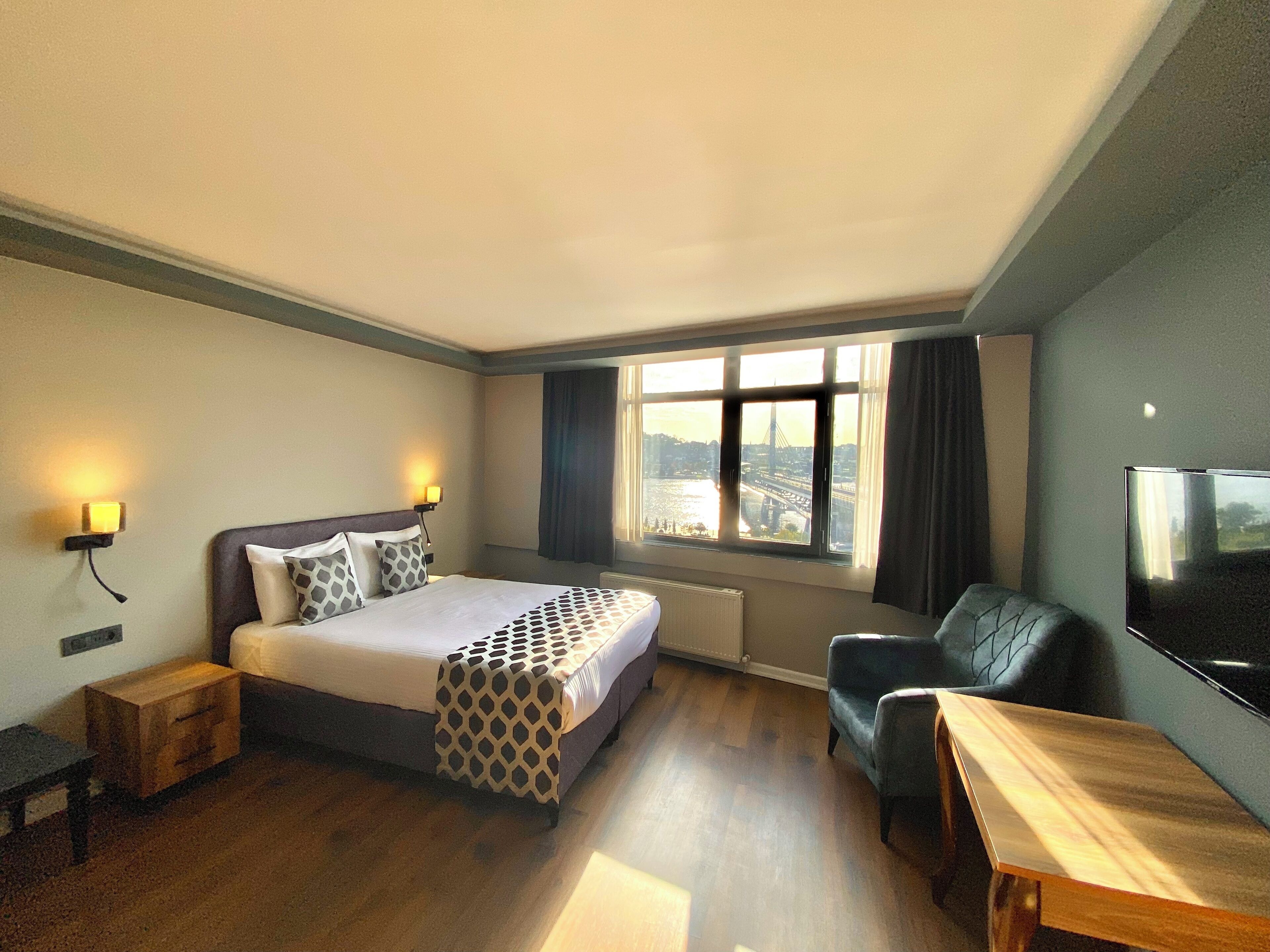 Habitación de hotel con cama, escritorio, silla, televisor y ventana con vista a la ciudad.
