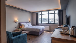 A modern hotel room with a large bed, a desk with a kettle, a chair, and a view of the city through large windows. - The Han Residence Halic Hotel (Istanbul)