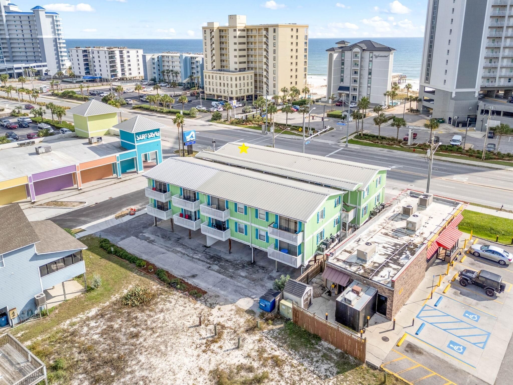 A multi-story hotel with a flat roof, located near a beach and parking area.
