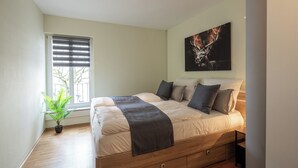 Ein Schlafzimmer mit einem Bett, einem Fenster mit Jalousien, einer Pflanze und einem Bild an der Wand.