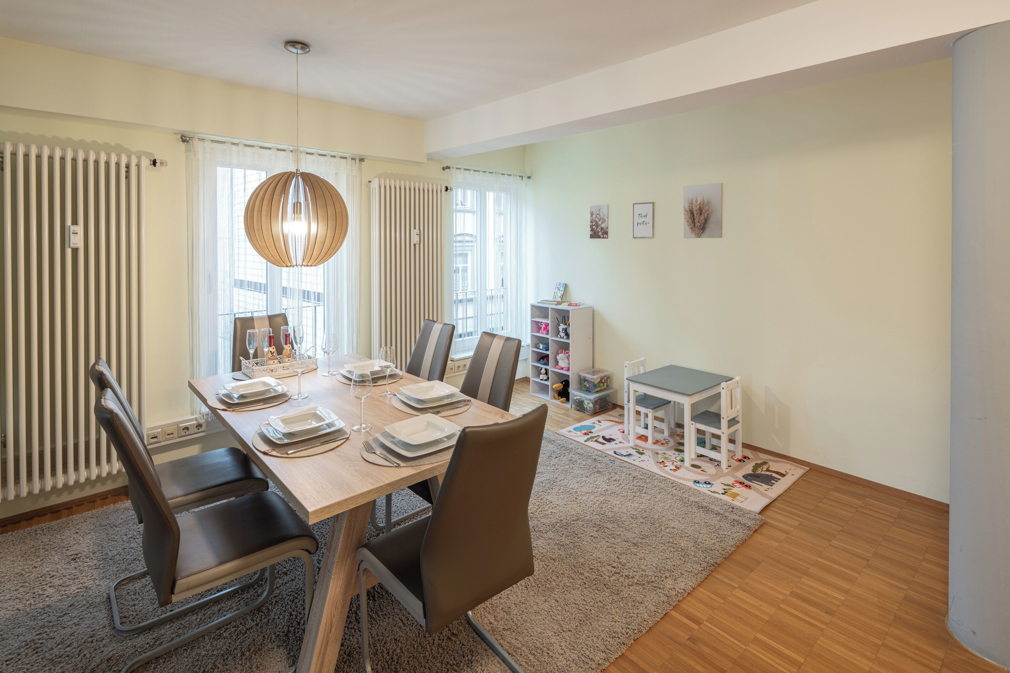 A dining area with a wooden table set for four, surrounded by chairs, a chandelier, and a radiator.