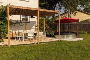 A backyard patio with a wooden pergola, a table with chairs, a red umbrella, and a hot tub. - Modern home with an enclosed backyard with outdoor seating in North Austin (Austin)