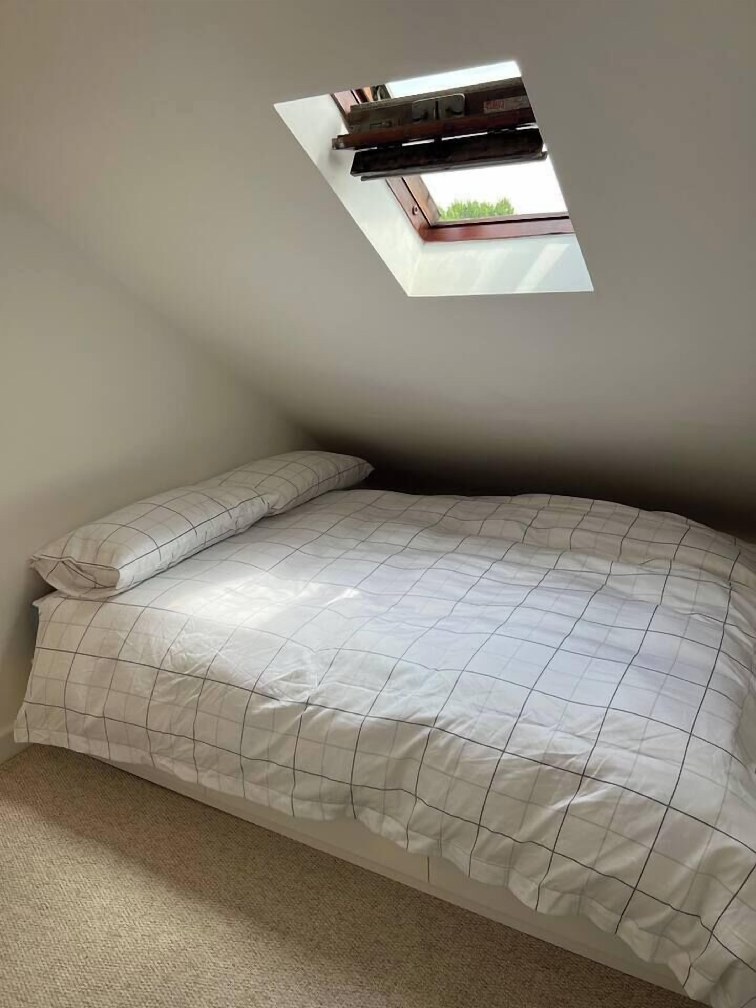 Un dormitorio pequeño con una cama individual, un tragaluz y vistas al exterior.