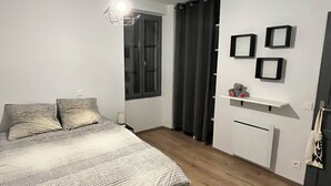 Une chambre à coucher comprenant un lit, une table de chevet, une commode, une fenêtre avec des rideaux et un luminaire suspendu.