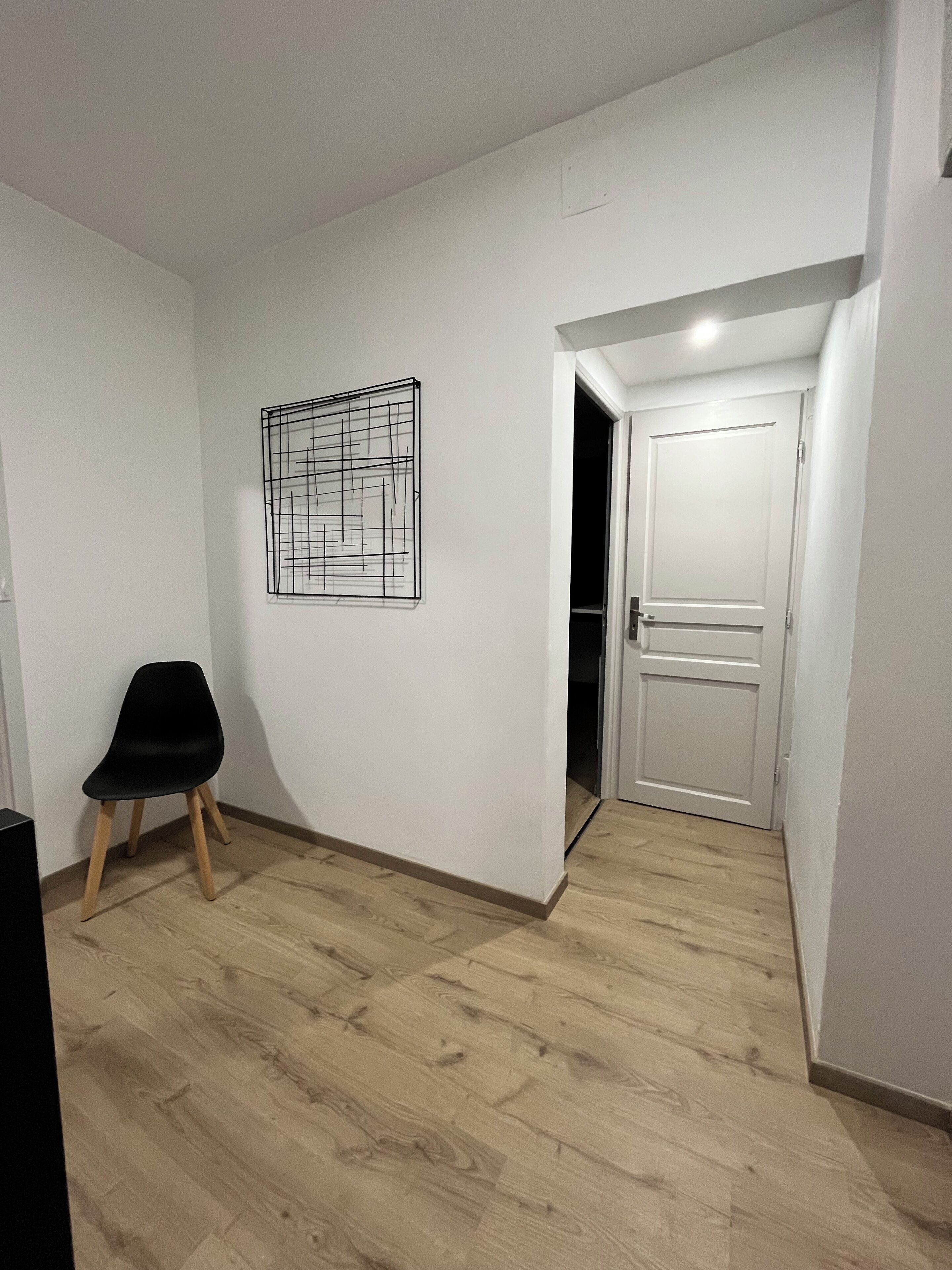 Una habitación con piso de madera, una silla negra, una puerta blanca y una obra de arte abstracta colgada en la pared.