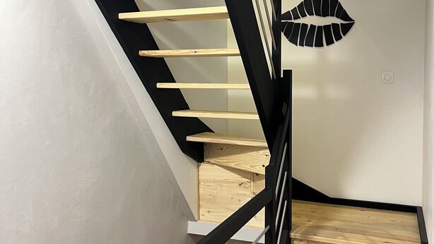 Un escalier en bois avec des rampes noires et une décoration murale représentant des lèvres.