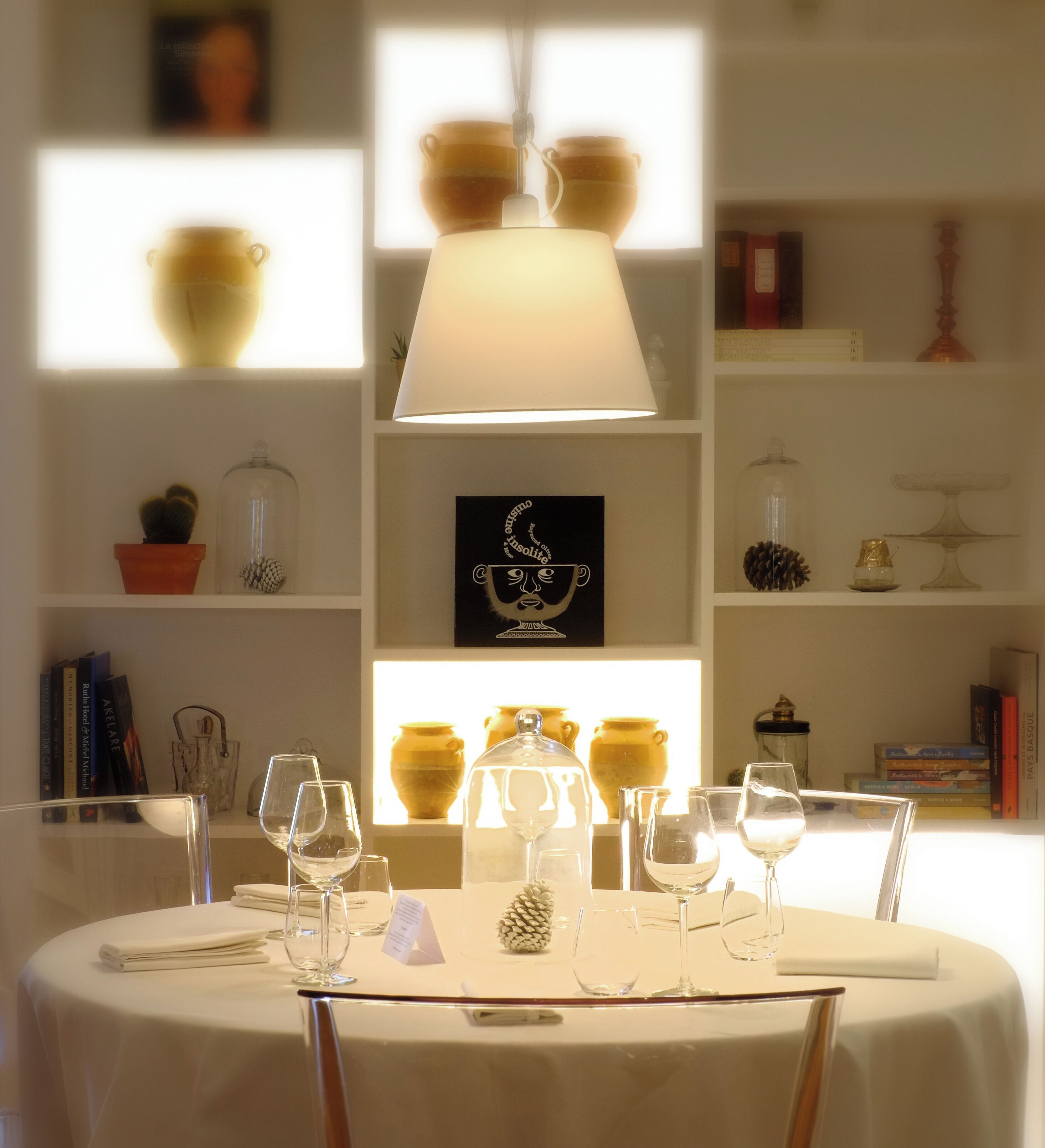 Une table à manger, agrémentée de verres à vin et d’un menu, est entourée d’étagères où sont disposés des objets décoratifs et des livres.