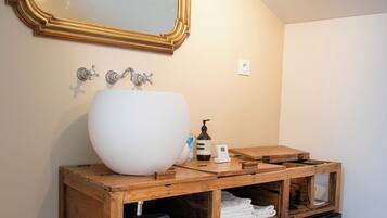 Un baño con un lavabo grande blanco, tocador de madera, un espejo con marco dorado y un refrigerador negro.