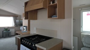 Eine kleine Küche mit Herd, Holzregalen, einem Tisch und einem Fenster.
