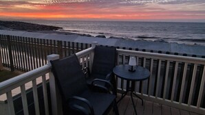 Eine Terrasse mit zwei Stühlen und einem kleinen Tisch, mit Blick auf eine felsige Küstenlinie bei Sonnenuntergang.