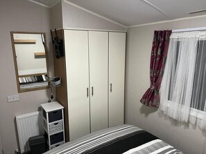 Un dormitorio con cama, armario, radiador y ventana con cortinas.