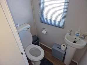 Un baño pequeño con inodoro, lavamanos, cubo de basura y ventana con persianas.