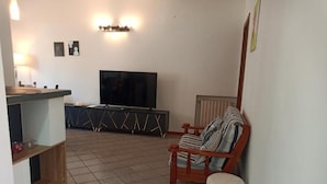 A living room with a TV, a wooden chair, a small ottoman, and a tiled floor.