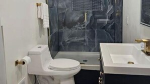 A modern bathroom with a marble shower wall, a white toilet, and a vanity with a sink. - Scotty's sunny spot (Doniphan)