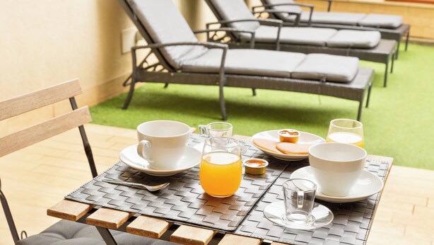 Ein Tisch reichhaltig mit Frühstück zubereitet, darunter ein Glas Orangensaft, Tassen und Teller mit Speisen.