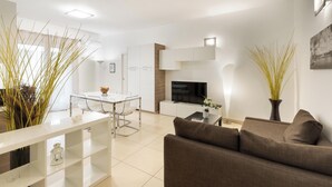 Ein modernes Wohnzimmer mit einer Couch, einem Esstisch mit Stühlen, einem Fernseher und dekorativen Pflanzen.