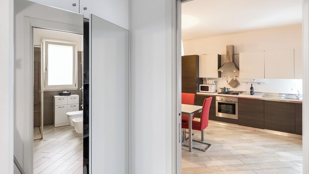 A modern kitchen with a central island, a dining area with red chairs, and a separate bathroom with a shower. - Suite 2 (Casamassima)