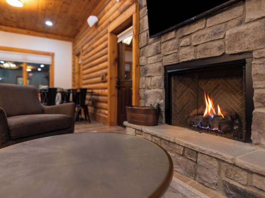 A cozy log cabin interior with a stone fireplace, a comfortable sofa, and a round table.