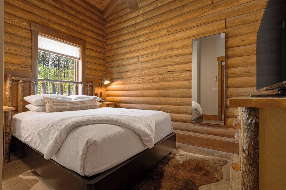 Una camera da letto in una baita di legno con un letto, un comodino, uno specchio e un televisore.